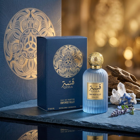 A bottle of Qissa Empower Valley Calm Eau de Parfum next to its blue packaging box, styled on a slate surface with decorative crystals, lavender, and driftwood against a warm golden bokeh background.