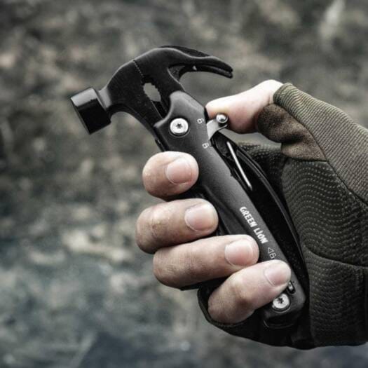 Multi-tool with hammer head held by a gloved hand against a blurred background
