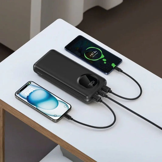 Two smartphones being charged by a power bank on a white surface.