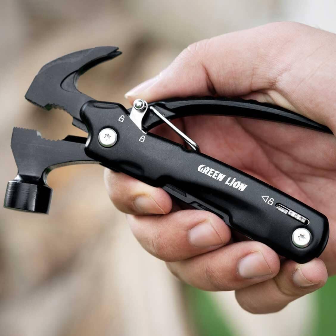 A hand holding a black multi-tool hammer with the brand name GREEN LION printed on the handle. The tool features a black body with silver metal accents and a small hammer head.