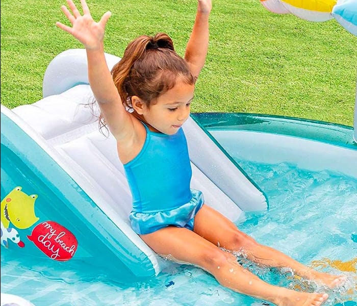 Child playing in a small inflatable pool with a slide on a grassy background