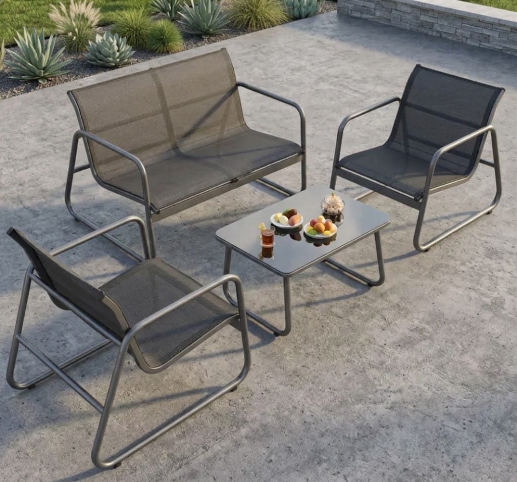 Four-piece outdoor patio furniture set including a loveseat, two armchairs, and a small rectangular coffee table, shown on a concrete patio with plants in the background.