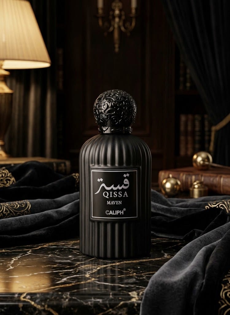 A black ribbed perfume bottle with a sculpted cap and a front label reading QISSA MATEN CALIPH, set on a dark marble surface with draped black fabric and warm ambient lighting in the background.