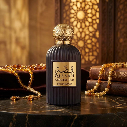 A dark purple ribbed perfume bottle with a gold cap and a gold label reading 'QISSAH GREATEST OUD LAU DE PARFUM', set on a marble surface with gold necklaces and books in a warm, ornate background.
